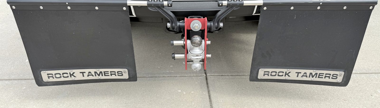 The Shocker Hitch Air pivot-point hitch flanked by two Rock Tamers mud flaps, mounted on the tow vehicle