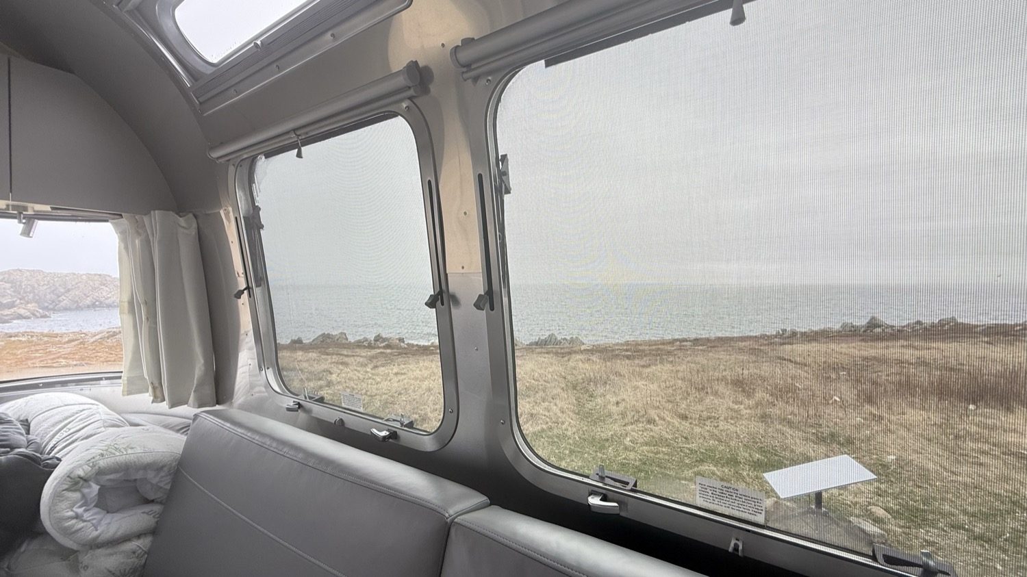 Looking out the Airstream's rear window at the ocean and grassy point beyond