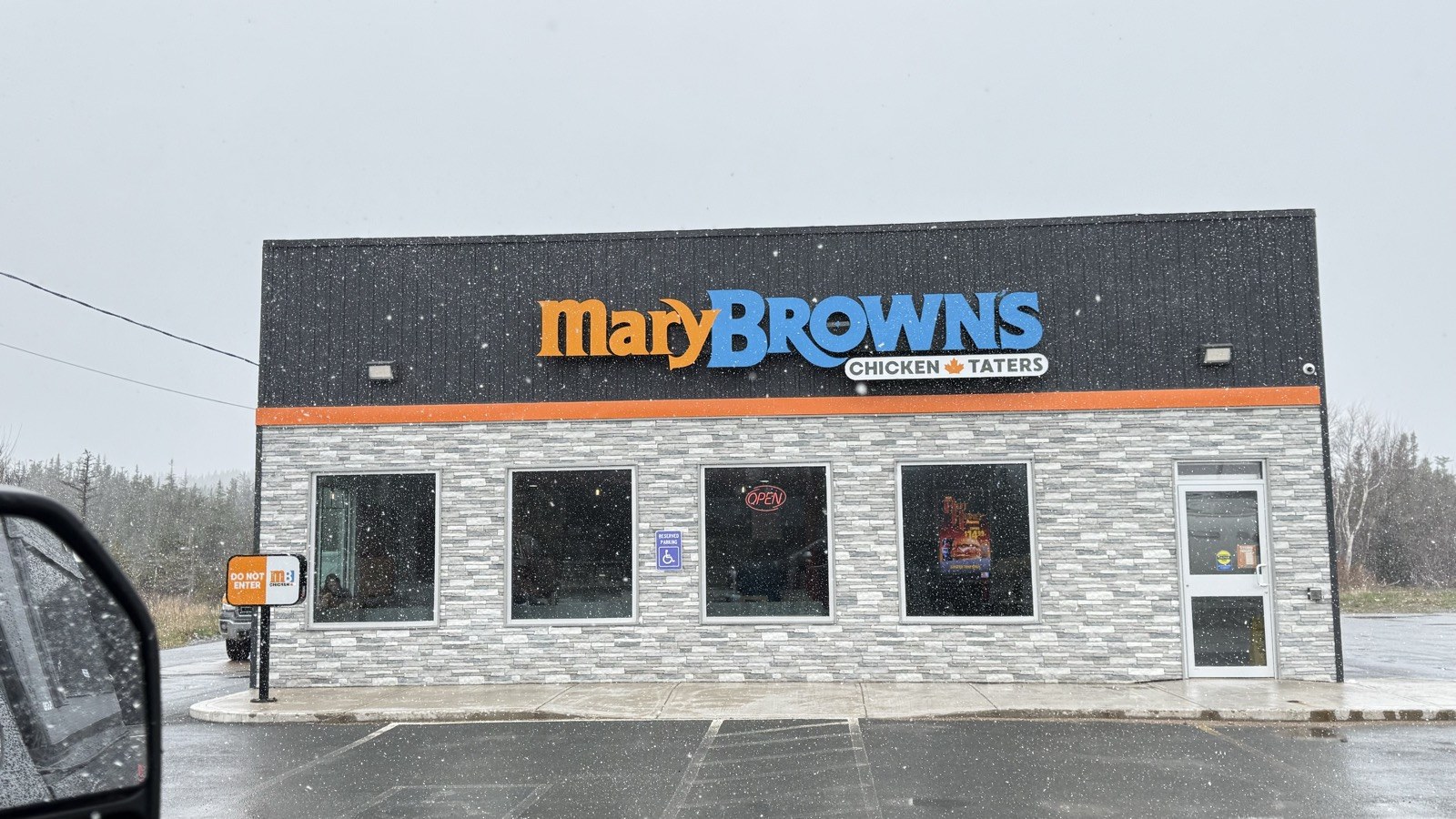 A Mary Brown's Chicken and Taters restaurant storefront, seen through the truck windshield during snowfall