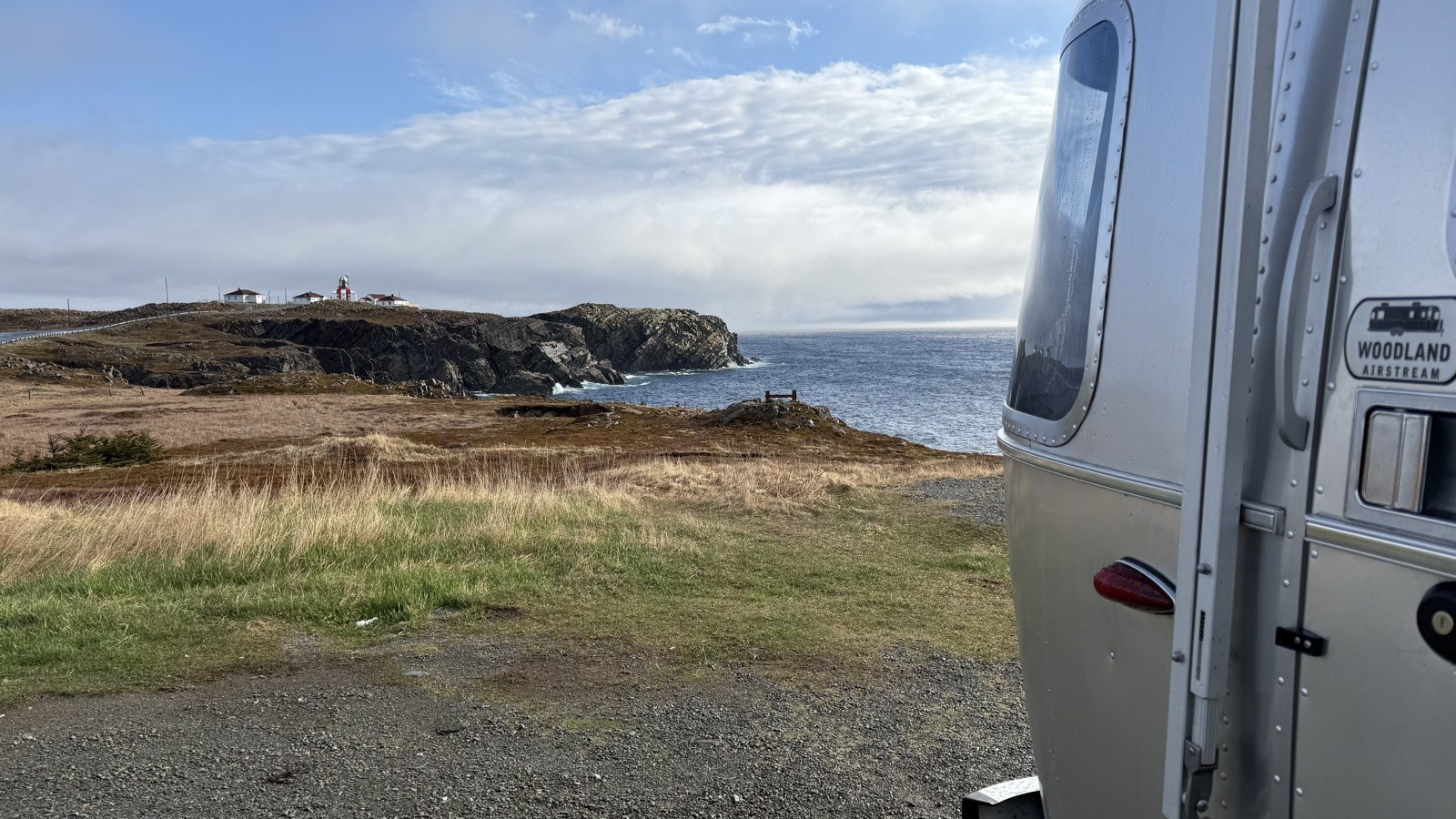 Our Airstream, with the Woodland Airstream badge visible, at the original pull-off on a sunny morning, with the lighthouse across the water