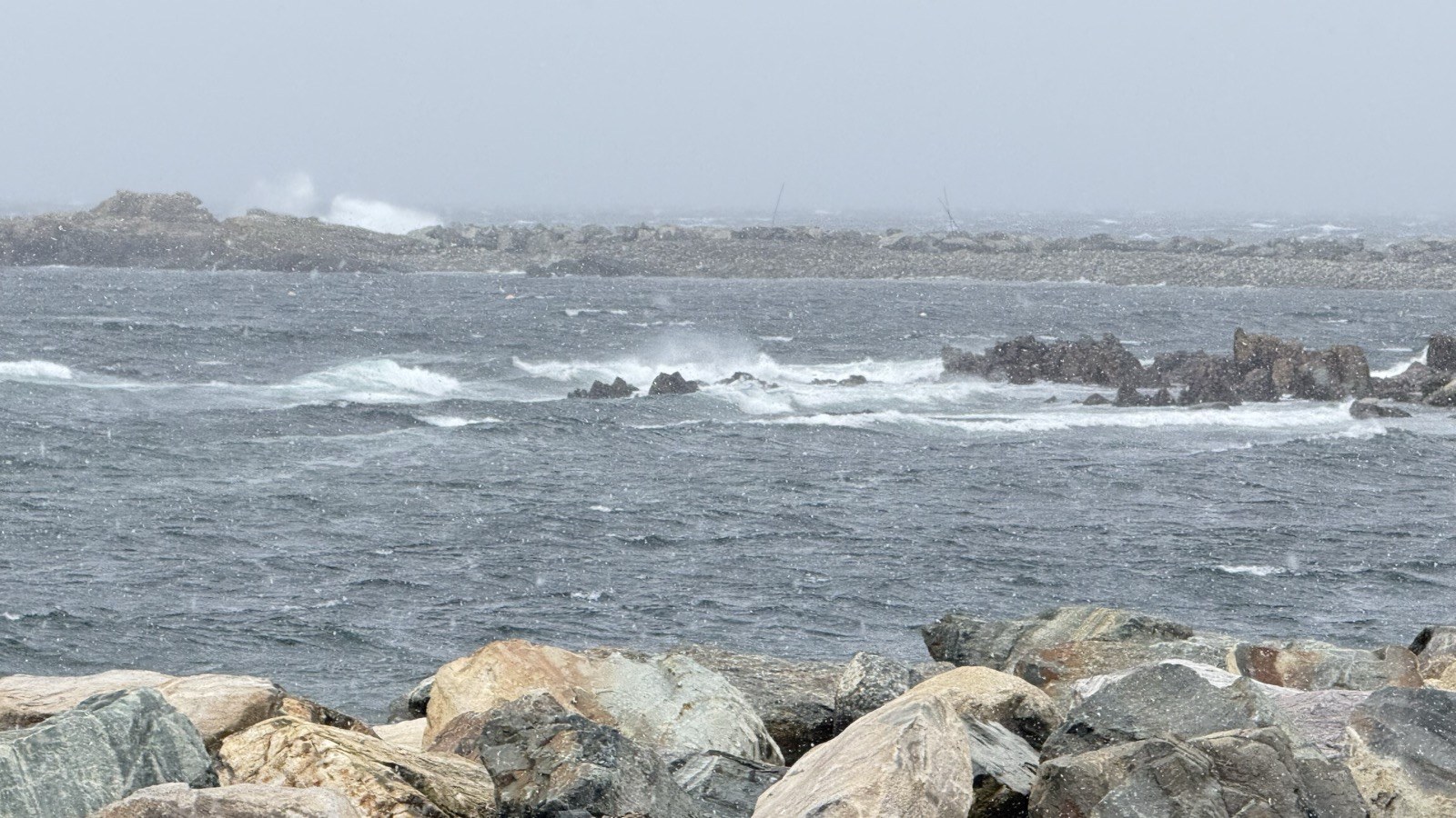 Waves crashing over rocks along the coast during snowfall and high wind