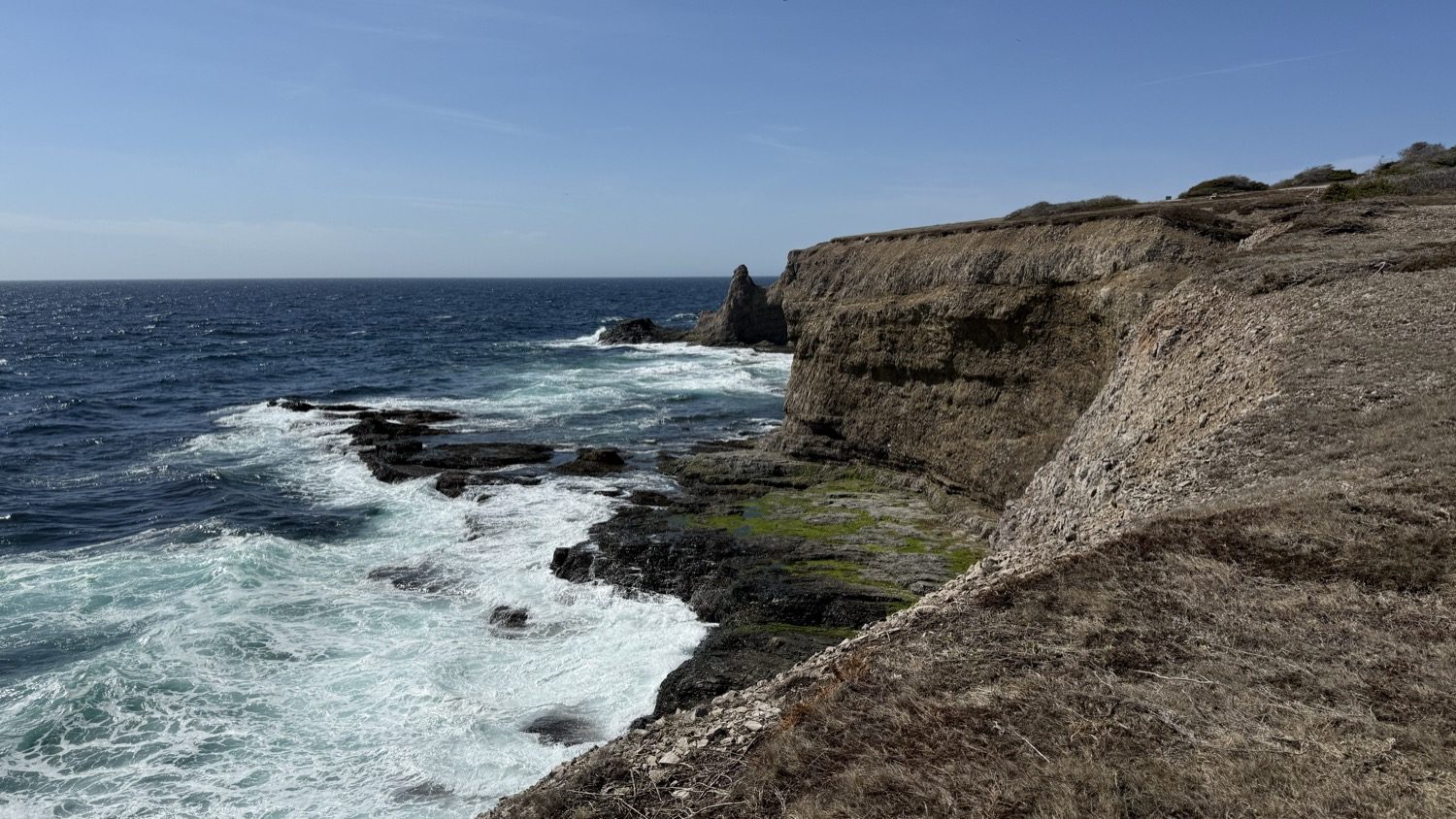 A rock sea stack at the base of the cliffs at Boutte du Cap Park, with waves breaking around it