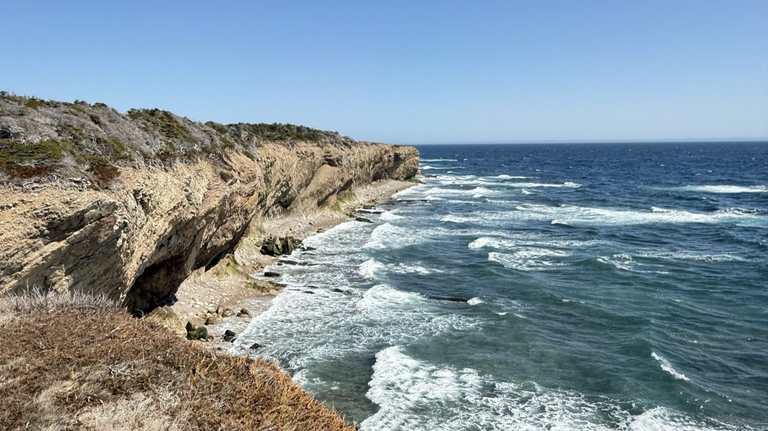 The rugged cliffs of Cape St. George dropping to a rocky beach, with waves rolling in