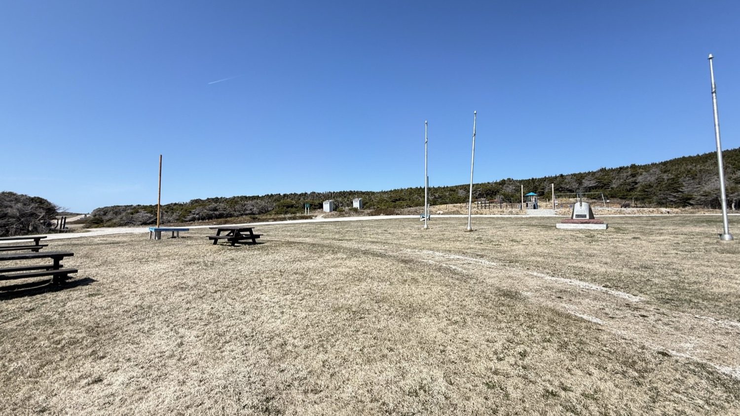 The open grounds at Boutte du Cap Park, with flagpoles and the Acadian monument set against the tree line
