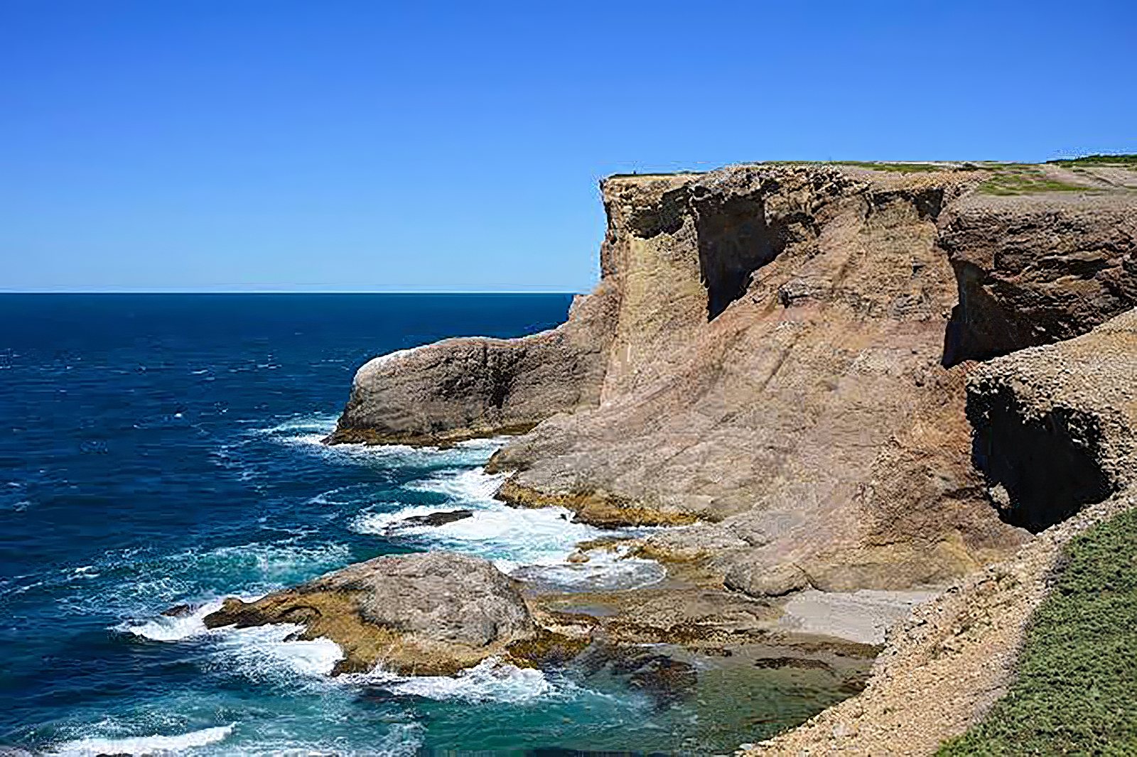 The Boot, a large rock formation at the base of the cliffs at Boutte du Cap Park, with waves breaking around it