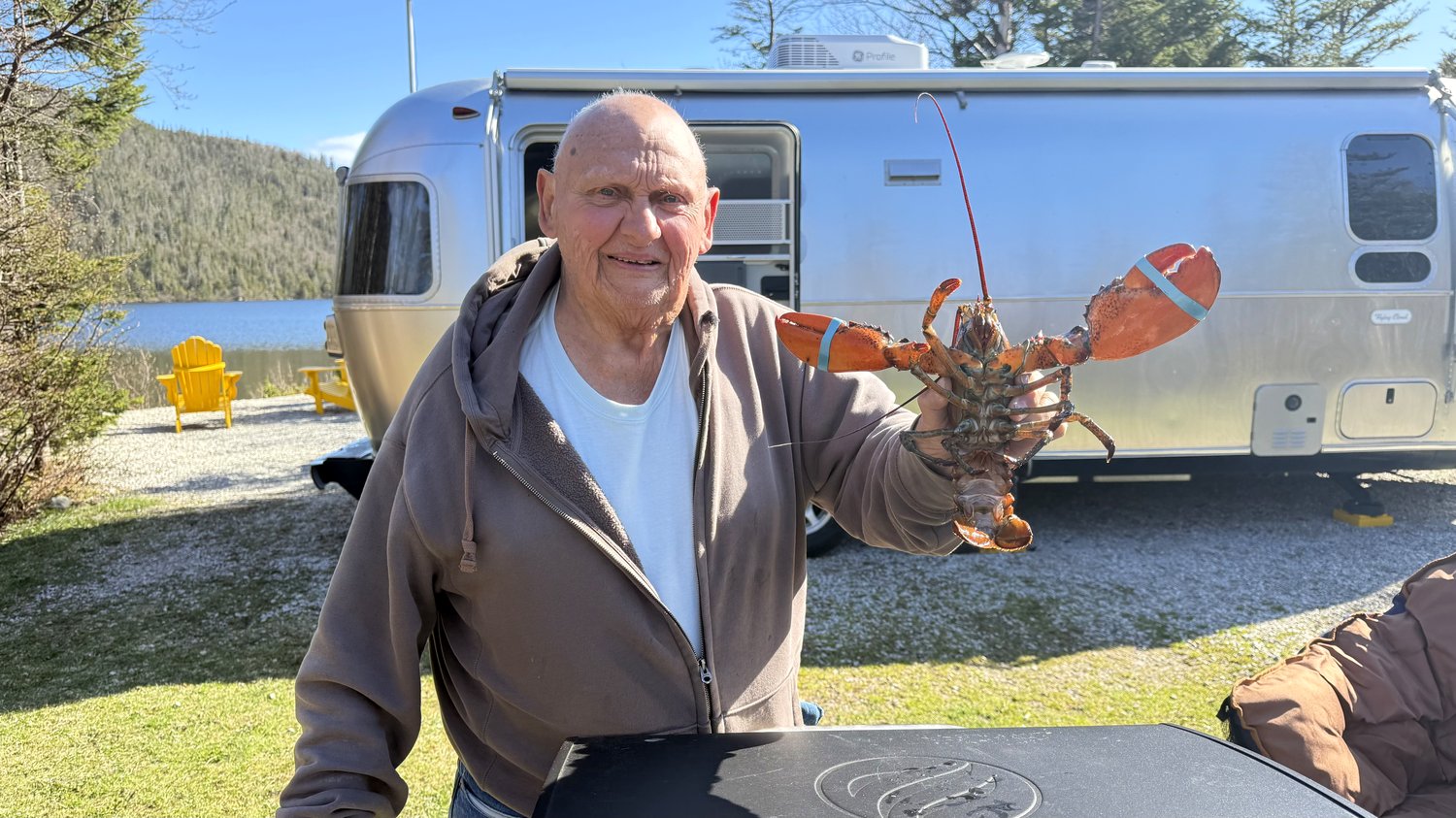 Heather's dad holding up a fresh-caught lobster back at the campsite, with the Airstream in the background