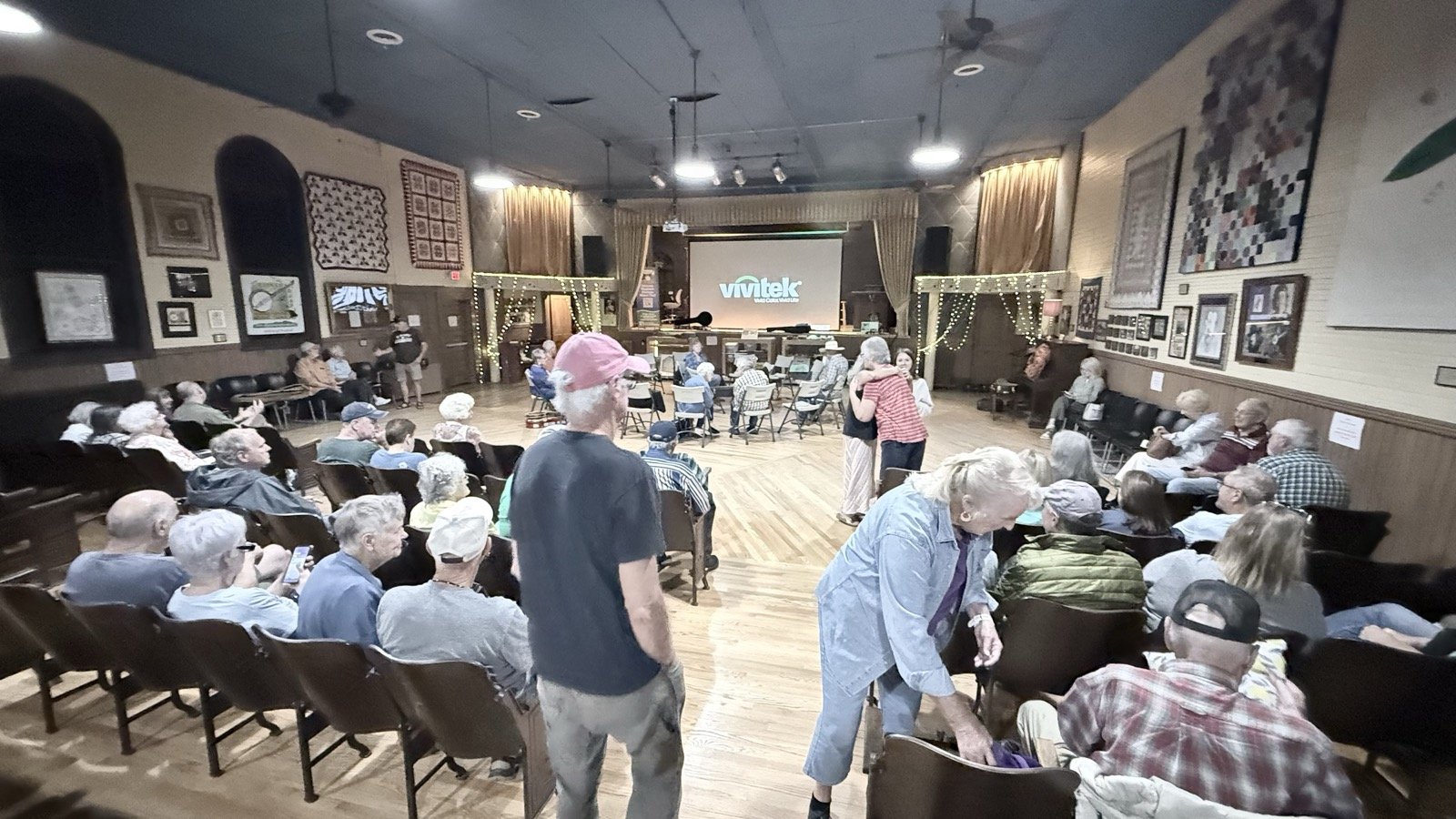 Inside the Fries Theatre hall before the music, with a circle of chairs at the far end, seating along both sides, and quilts hung on the walls