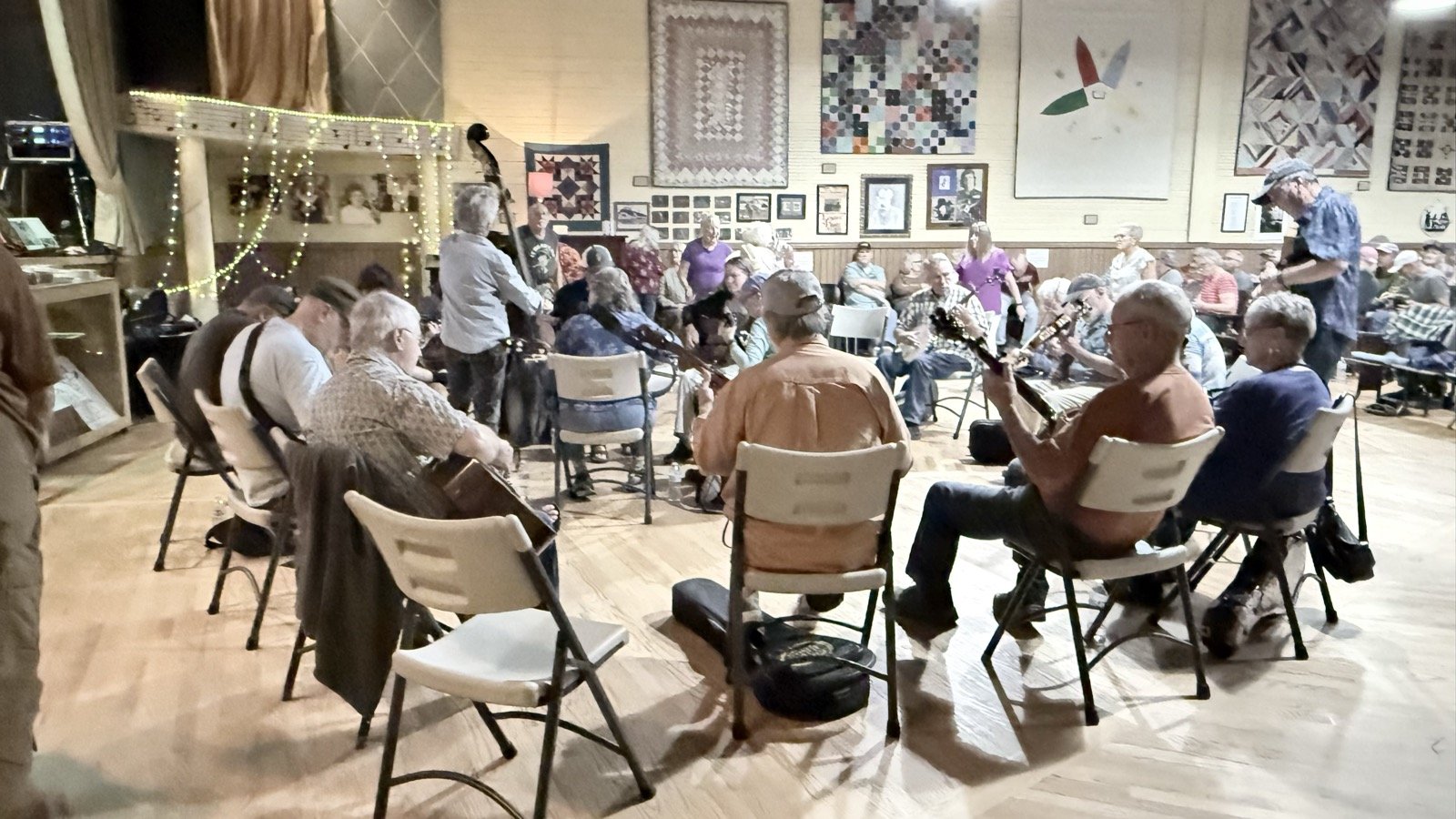 Musicians seated in a circle on the Fries Theatre dance floor with banjos, guitars and an upright bass during the Thursday Night Jam