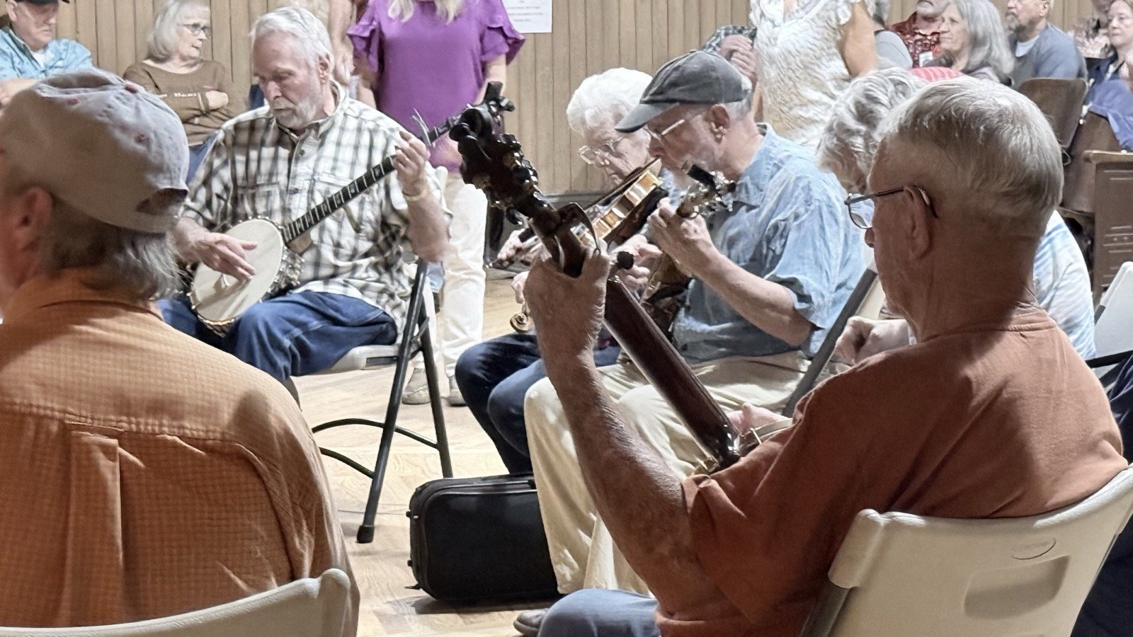 Close-up of musicians in the circle playing a banjo and other string instruments during the Thursday night jam