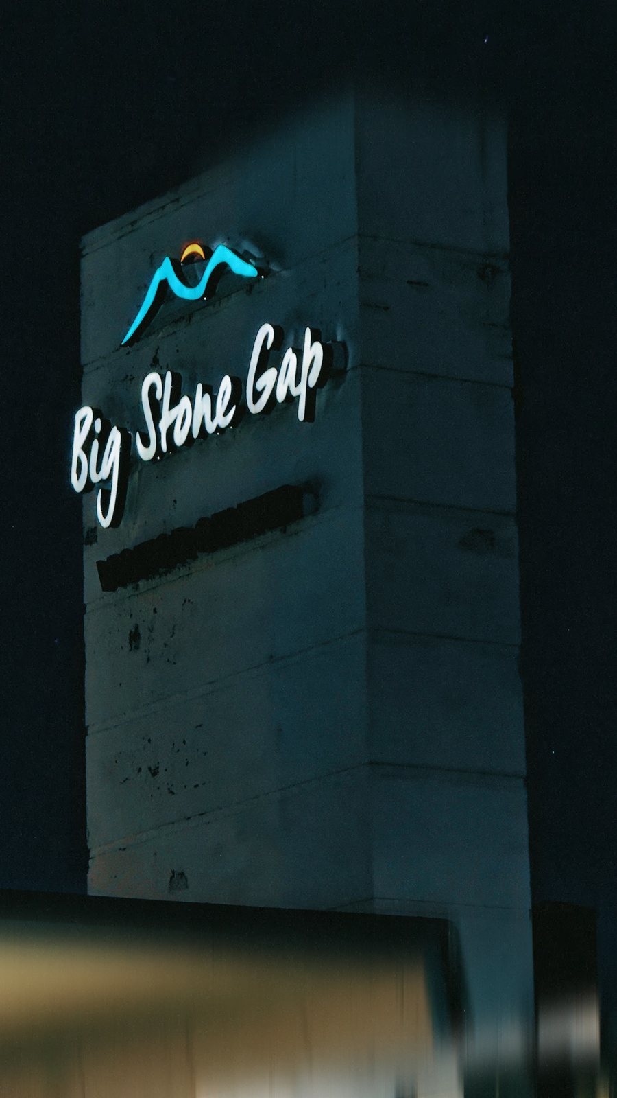 A lit sign tower at night reading Big Stone Gap, with a small mountain logo above the name