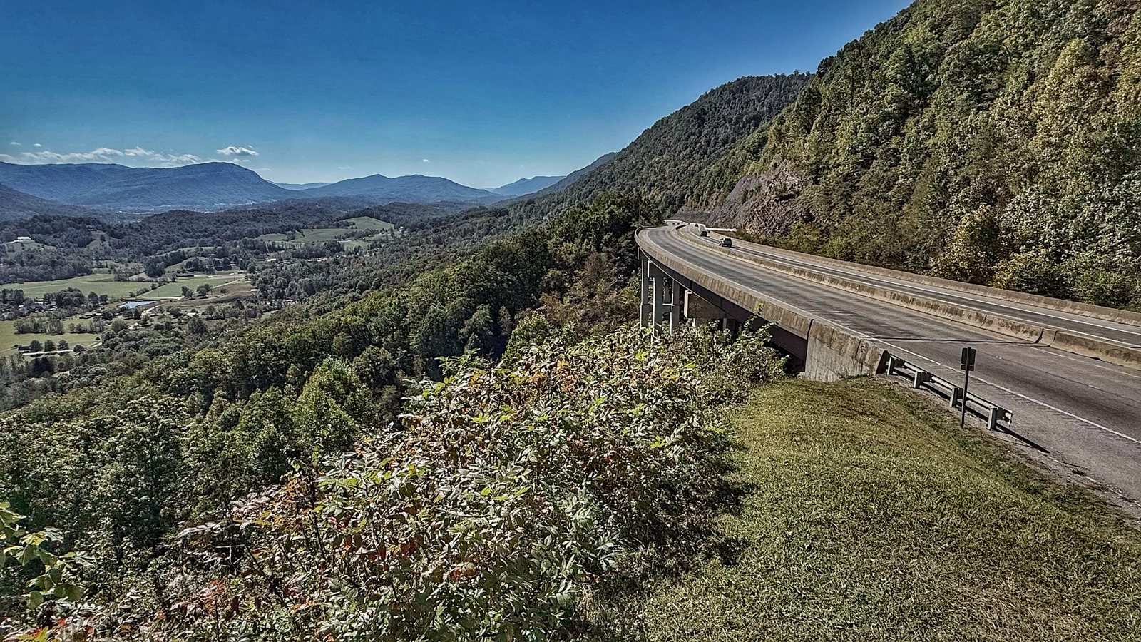 Looking down from the overlook at US 23 curving along the mountainside on a concrete bridge, with Powell Valley and blue mountains beyond