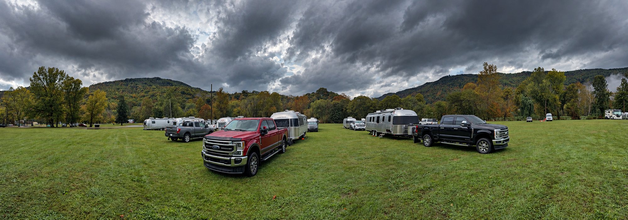 A wide view of the grass base camp on the last morning, with Airstreams and trucks on the lawn, fall trees, low mountain fog and heavy gray clouds