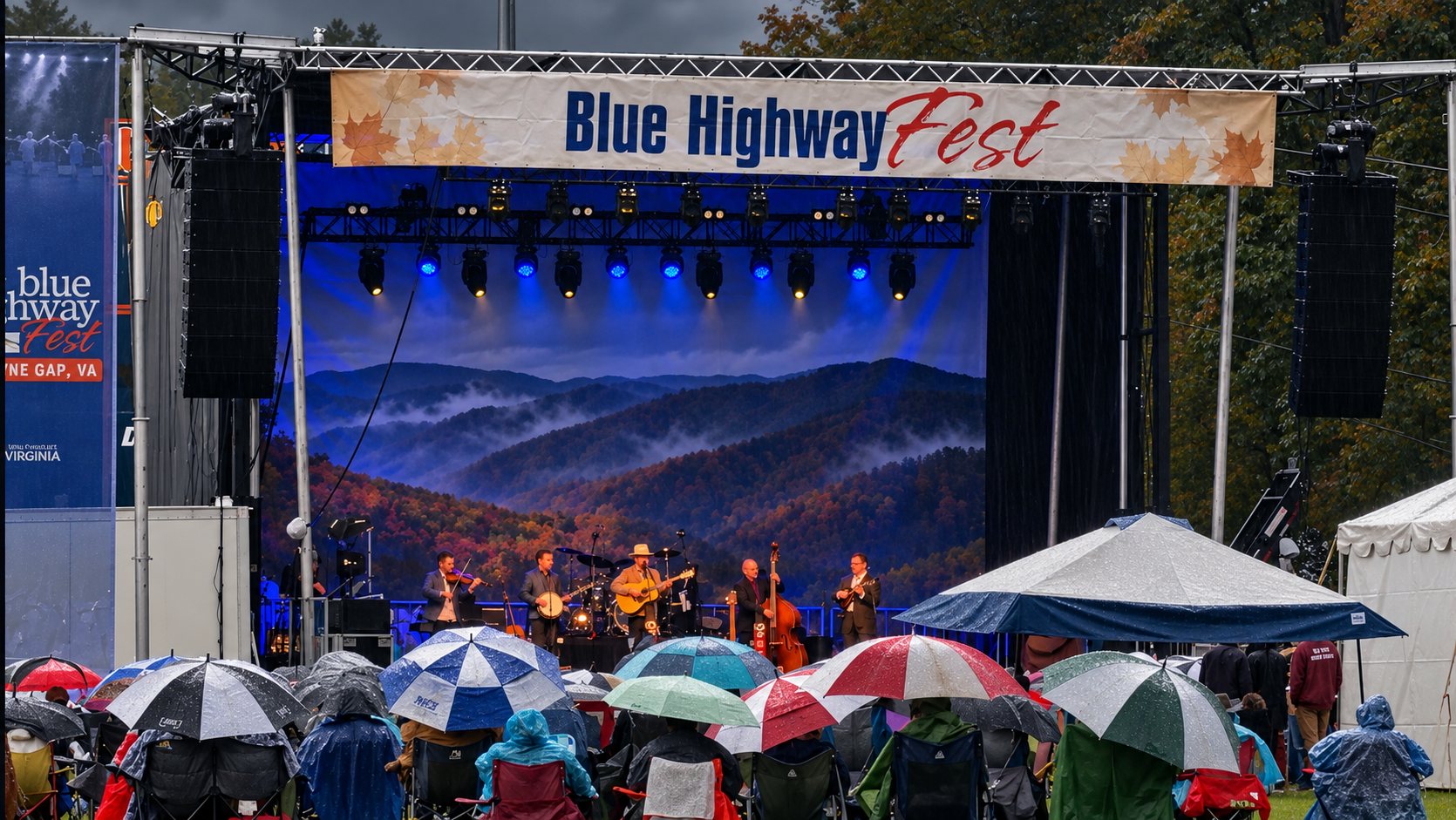 Dailey & Vincent on the Blue Highway Fest stage during a break in the rain, with a misty mountain backdrop and a crowd under umbrellas and ponchos
