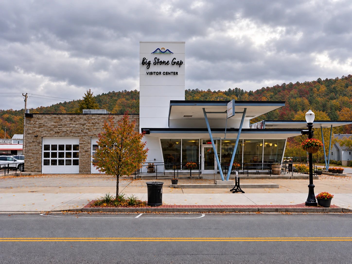 The Big Stone Gap Visitor Center, a retro white building with a slanted canopy and tall sign tower, with fall-colored hills and a cloudy sky behind