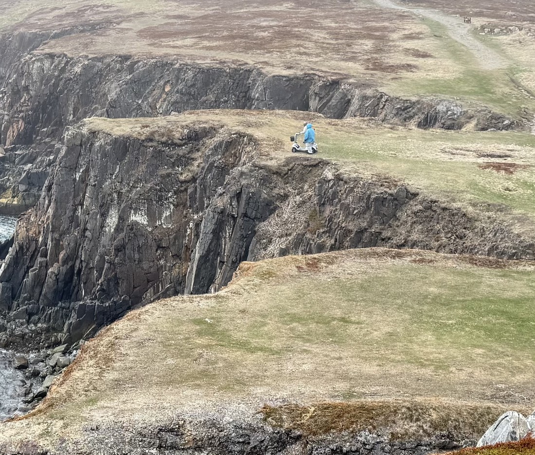 Heather walking beside her dad on his mobility scooter, right at the edge of a steep, unguarded cliff at Elliston