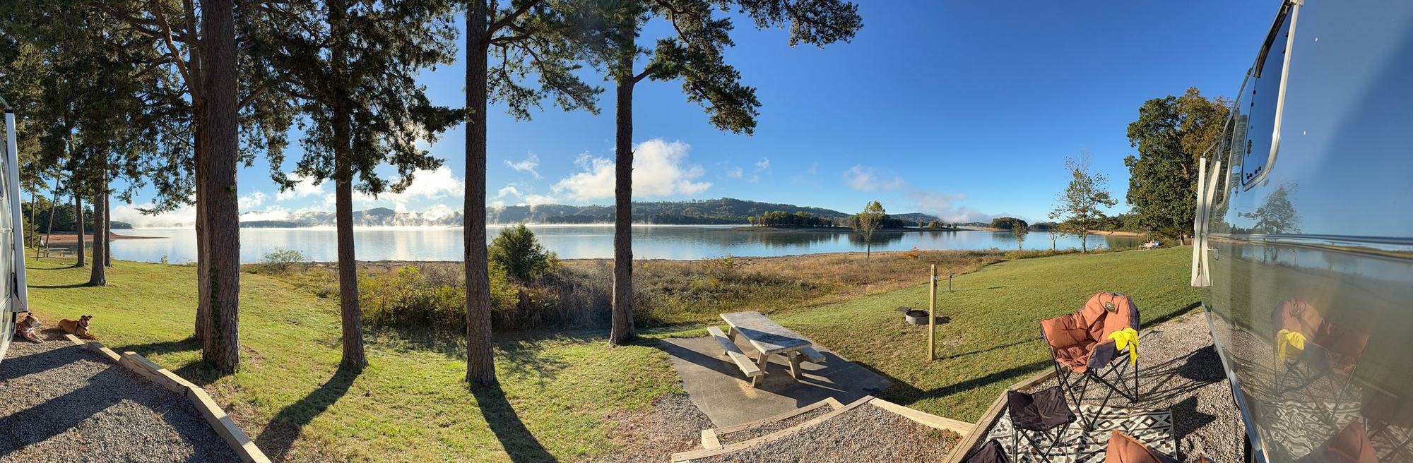 A wide view from our campsite across a grassy slope with camp chairs and a picnic table toward Norris Lake, with the Airstream at the right