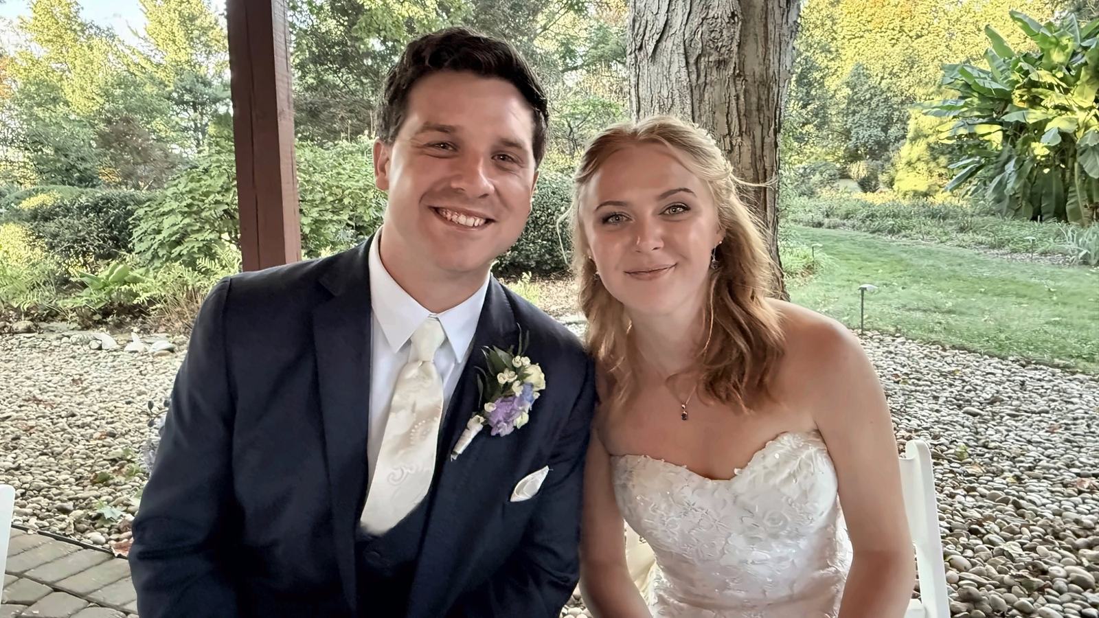 Ryan and his bride, Jessica, seated side by side and smiling under a pergola at the wedding venue