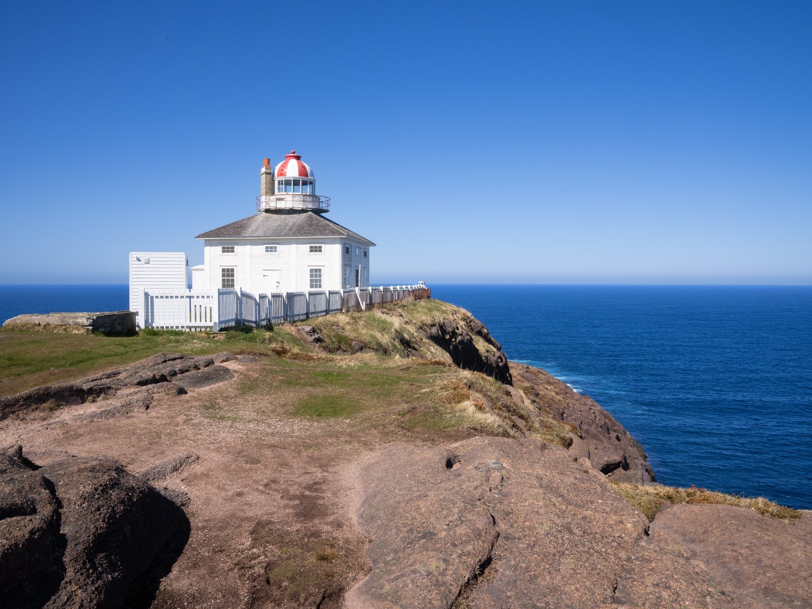 The old white Cape Spear lighthouse with a red-and-white lantern on a grassy cliff edge above the Atlantic
