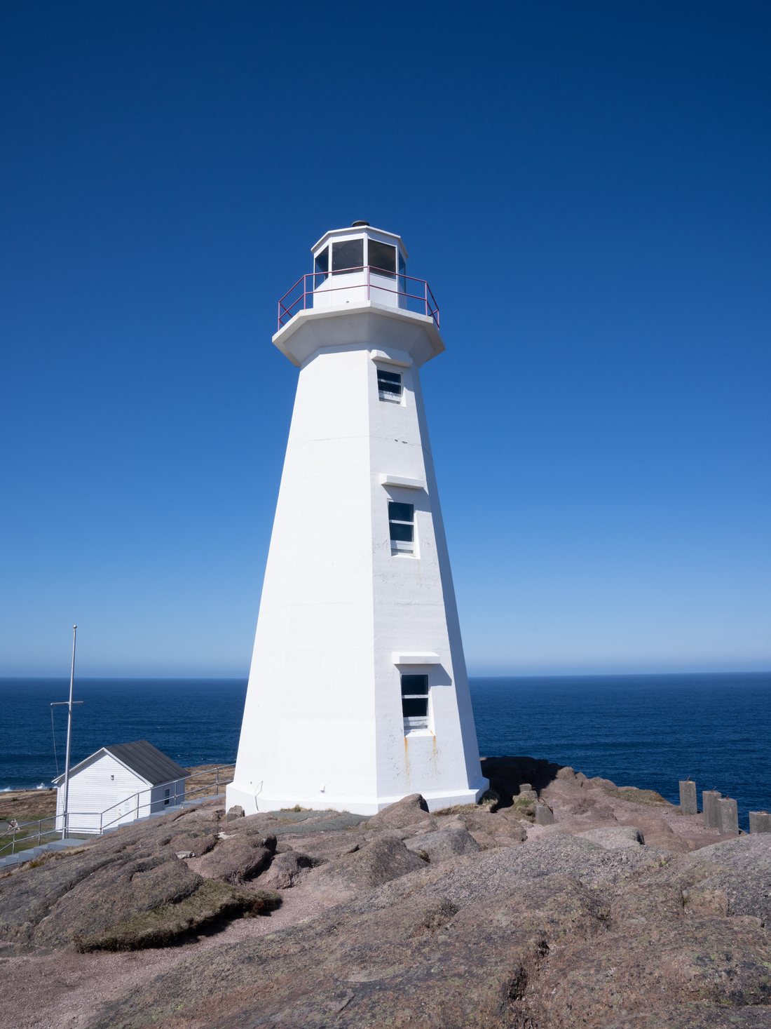 The tall white concrete Cape Spear lighthouse tower against a deep blue sky, with the ocean behind