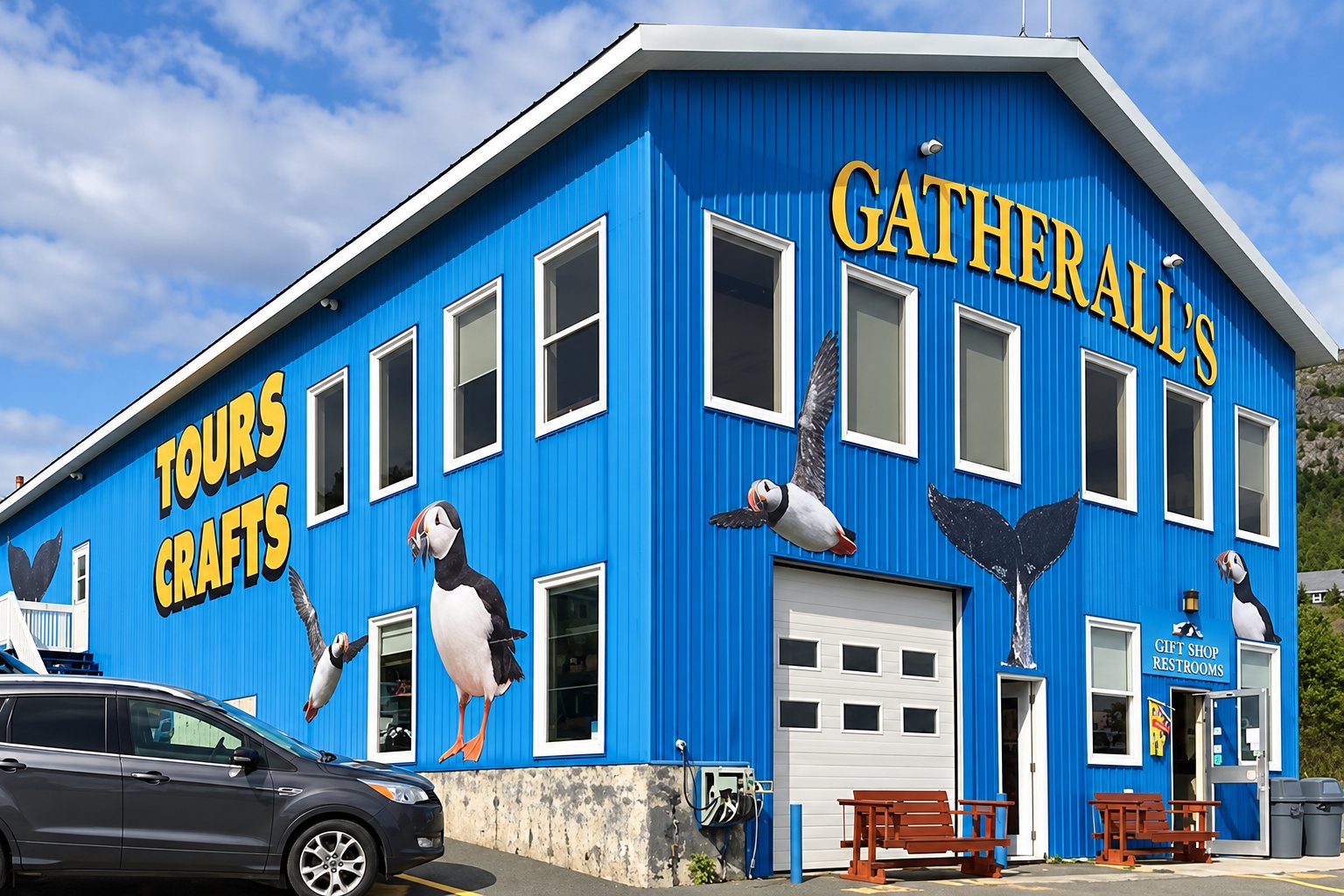 The bright blue Gatherall's building in Bay Bulls, with Tours and Crafts on the side and large painted puffins and a whale's tail on the walls