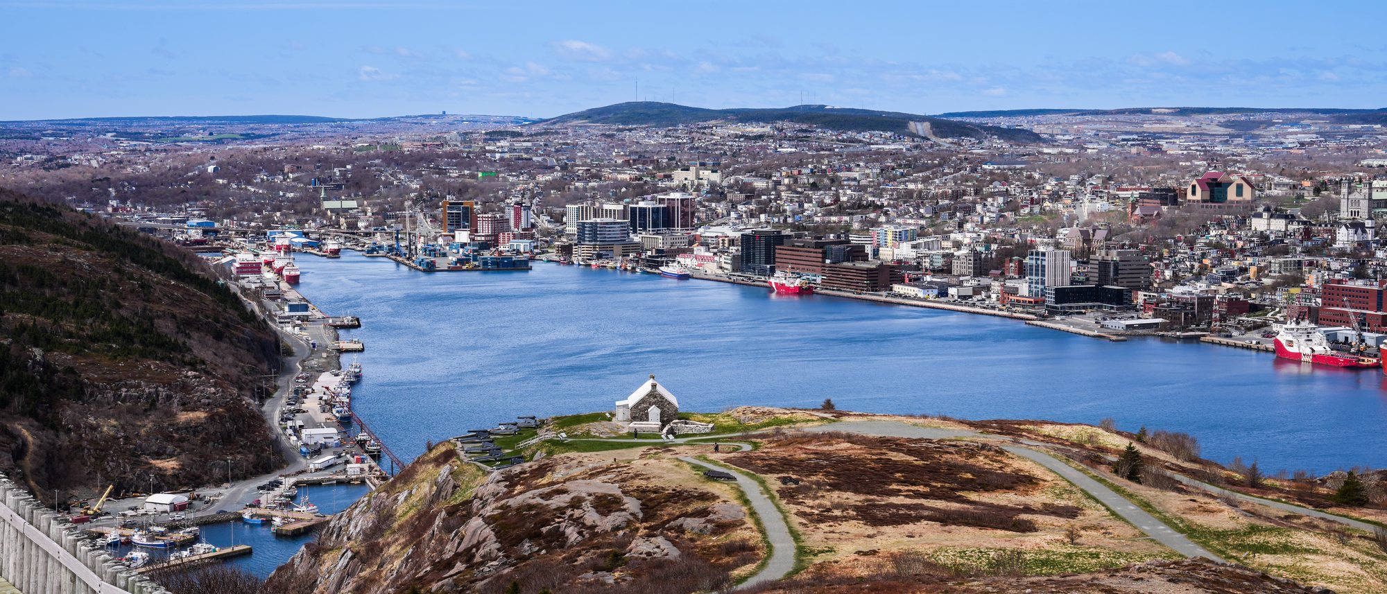 St. John's harbor and downtown from Signal Hill, with ships at the wharves and a small stone building on the headland