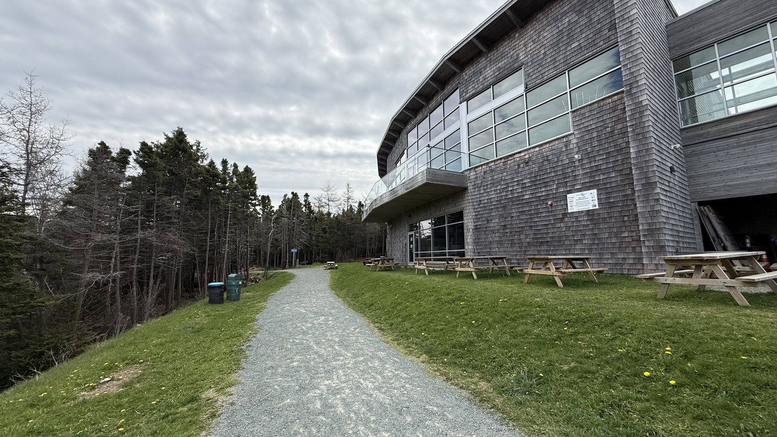 The shingle-and-glass interpretation centre above a gravel path and picnic tables on a green lawn