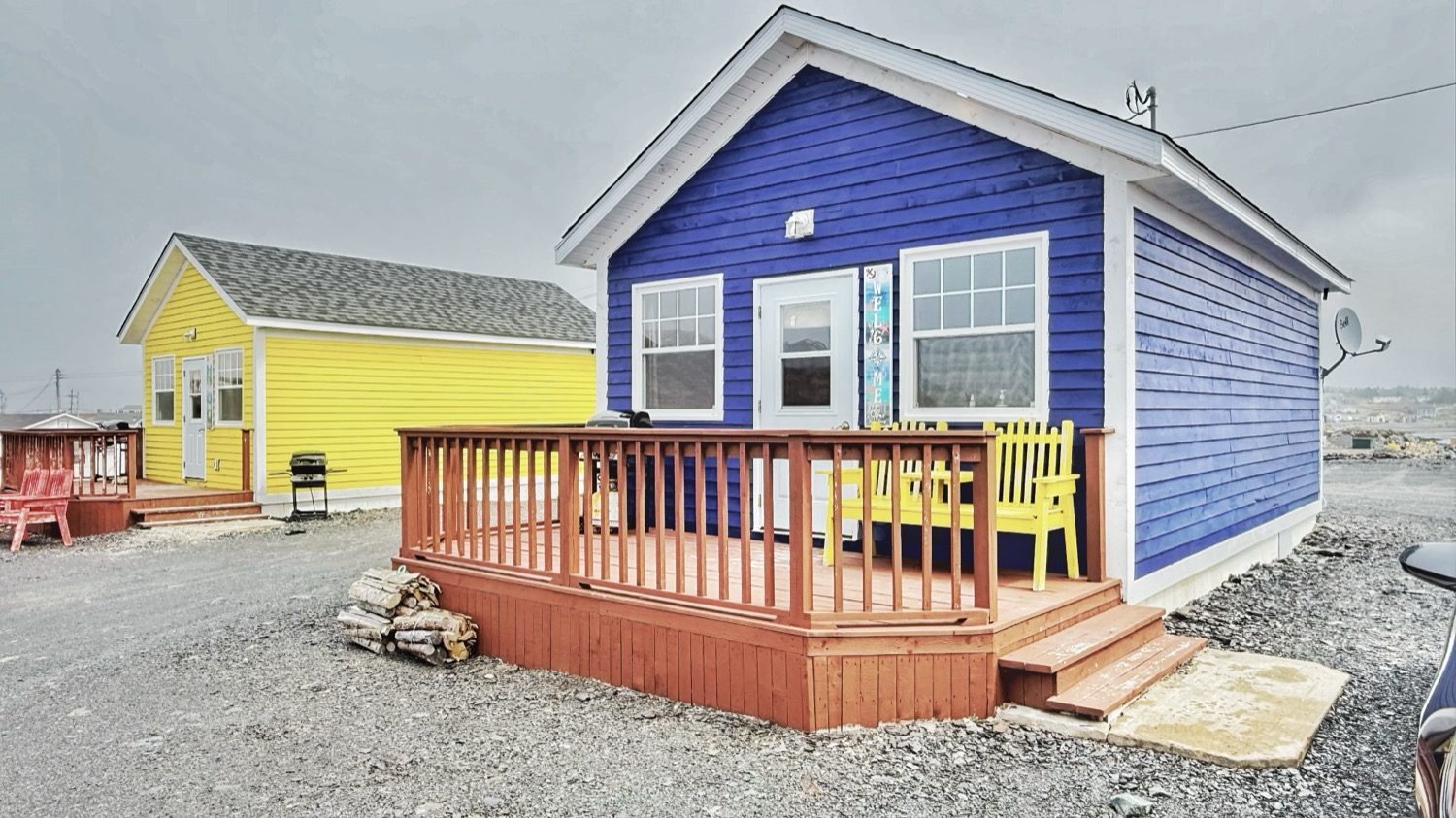 A blue house and a yellow house with orange-stained decks and a stack of firewood, under a gray sky