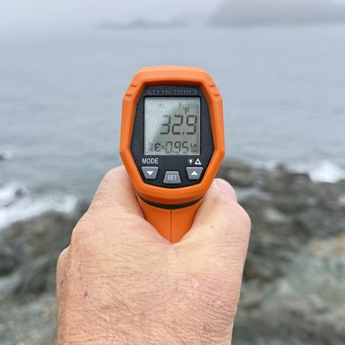 An orange infrared thermometer held in front of the ocean, reading 32.9 degrees Fahrenheit