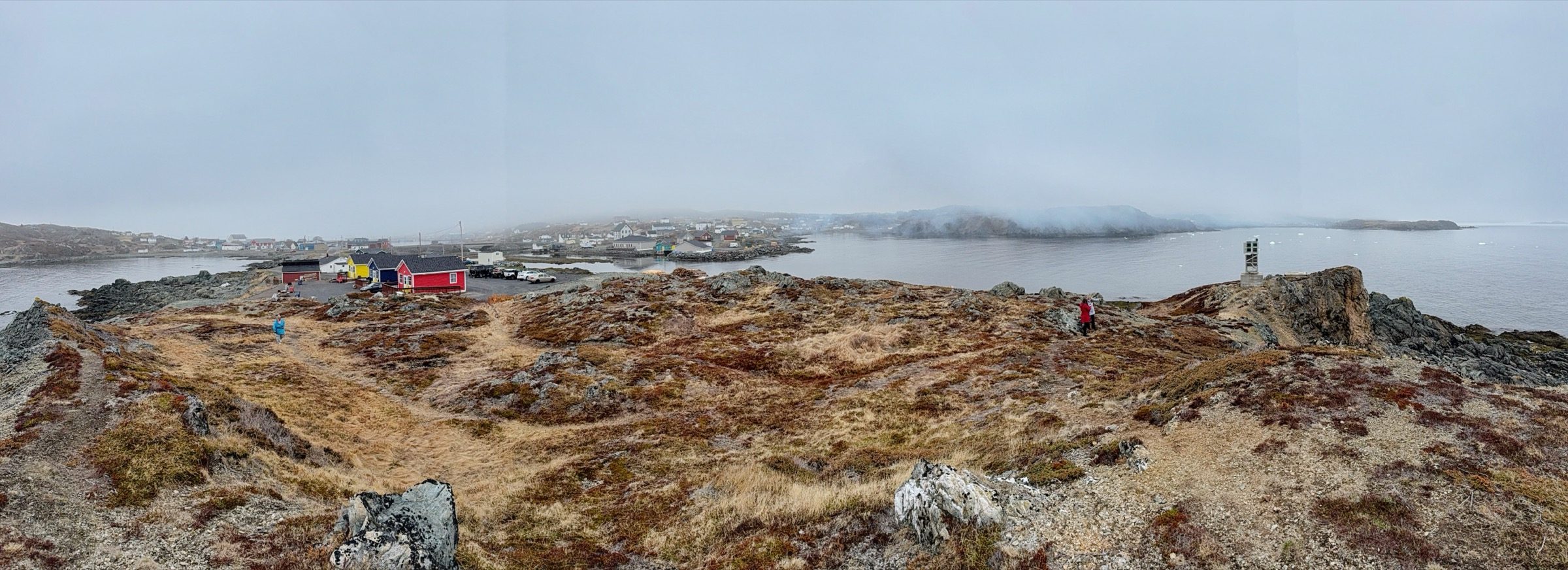 A wide panorama from a rocky point above Back Harbour, looking across the water to the village and fog-covered hills
