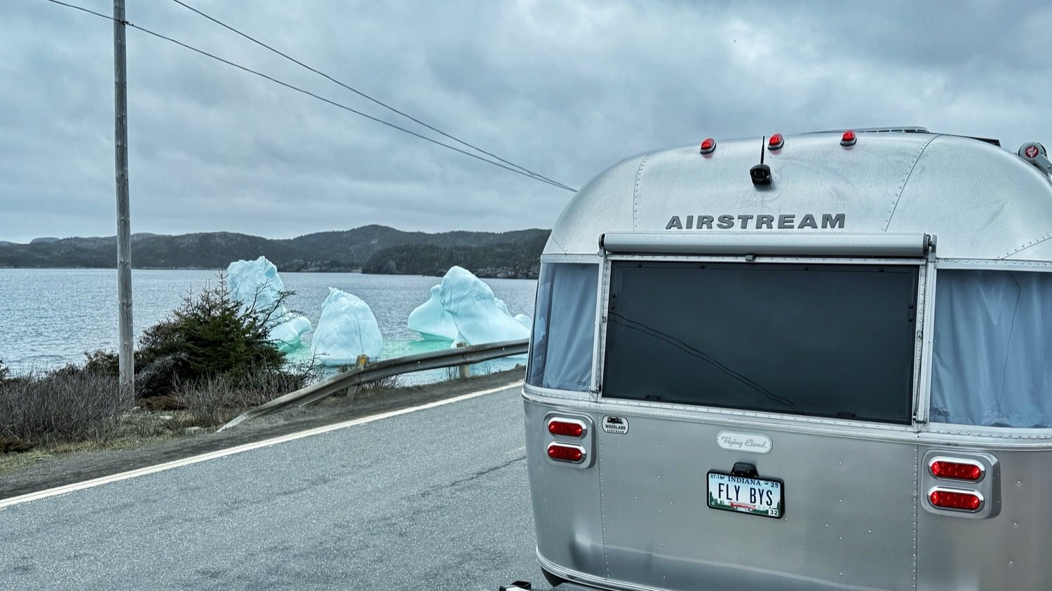 The back of our Airstream parked on a roadside, with pale-blue ice floating just beyond the guardrail