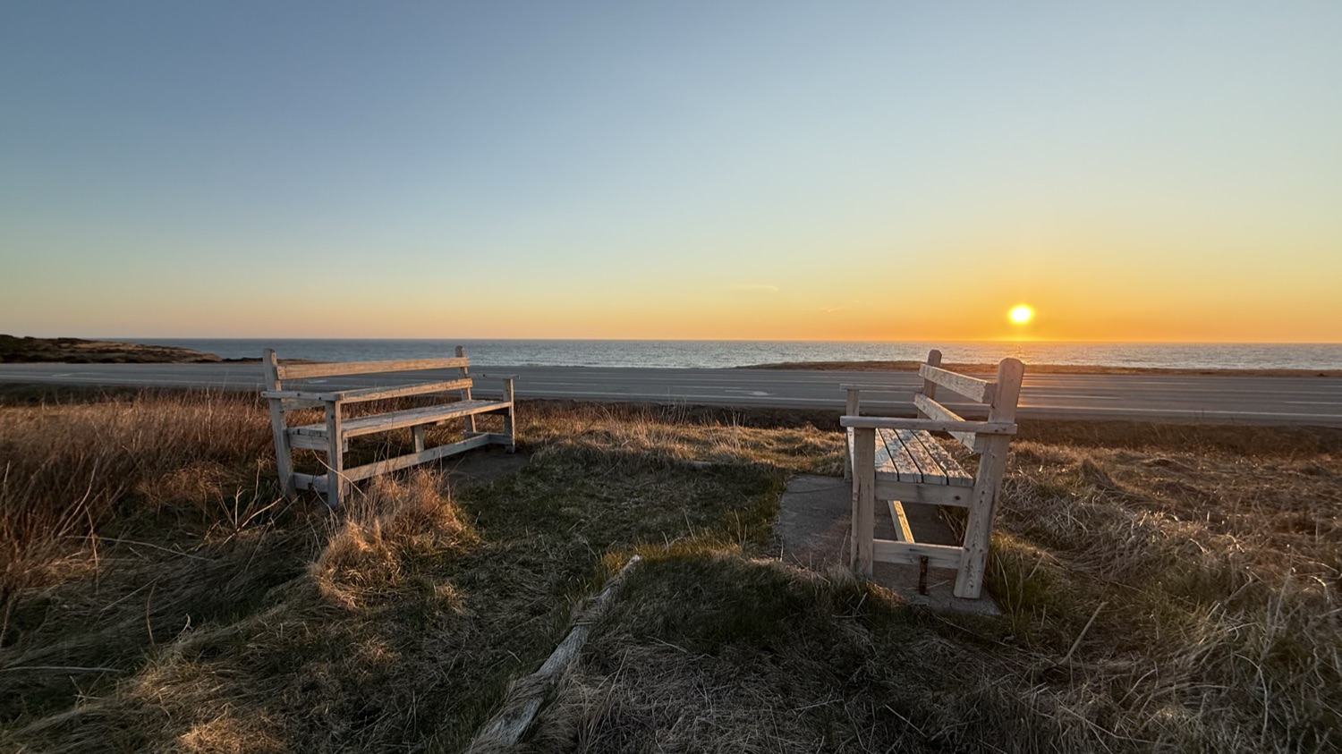 Two weathered wooden benches facing the ocean at Wreckhouse as the sun sets over the water