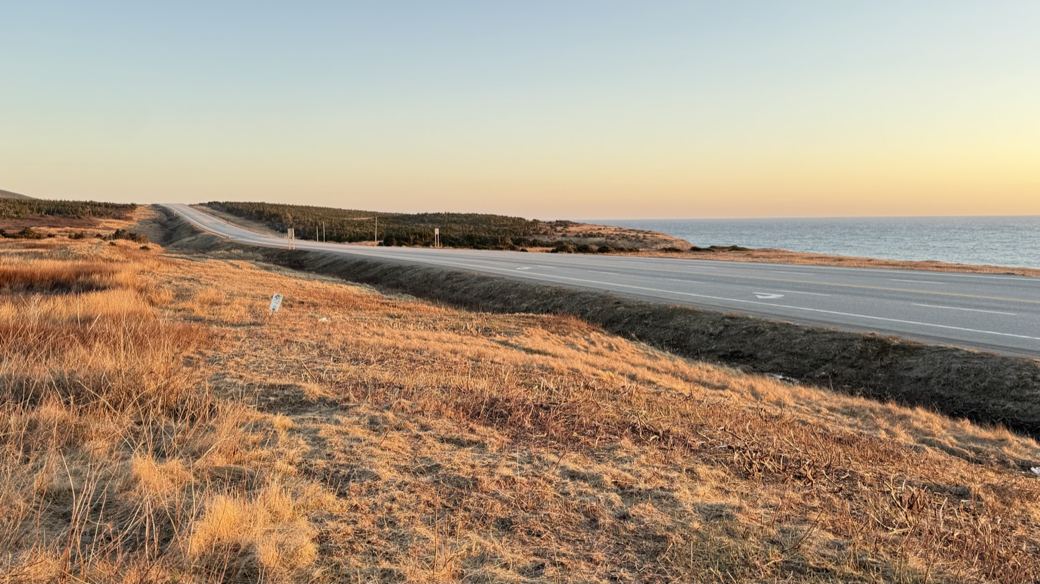 The Trans-Canada Highway curving along the Newfoundland coastline near Wreckhouse at golden hour, empty of traffic