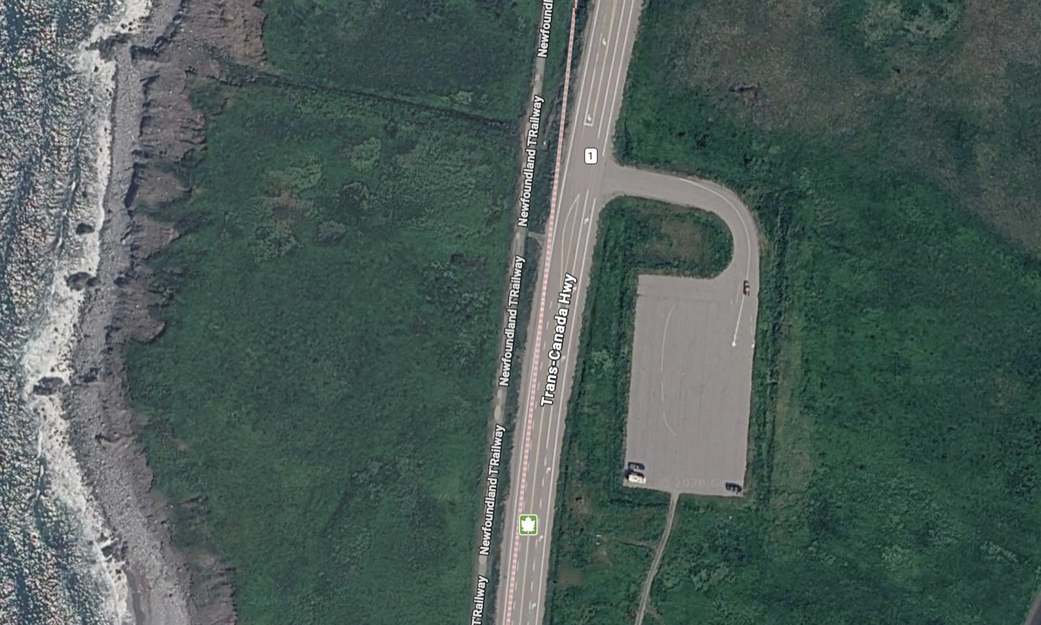Aerial view of the Wreckhouse parking area beside the Trans-Canada Highway, with the old railway bed running alongside it and the ocean just beyond