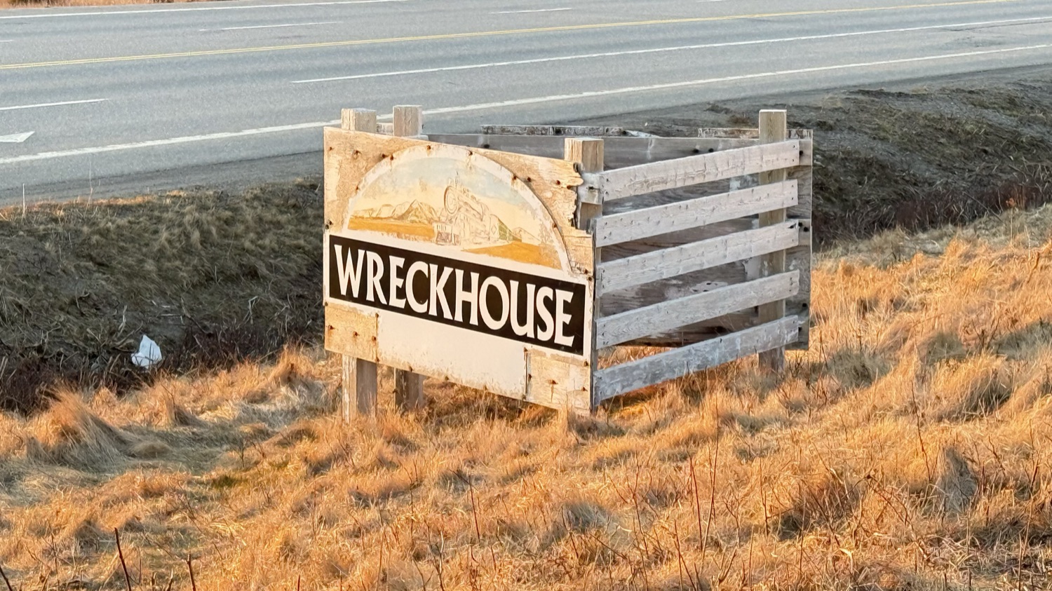 The weathered wooden Wreckhouse road sign beside the highway, with a small illustration of a steam train worked into the artwork