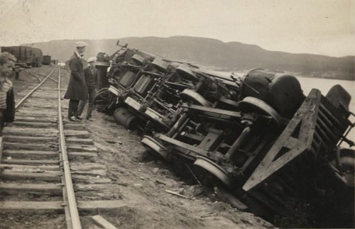 An old photograph of a train lying on its side beside the tracks at Wreckhouse, with onlookers standing nearby