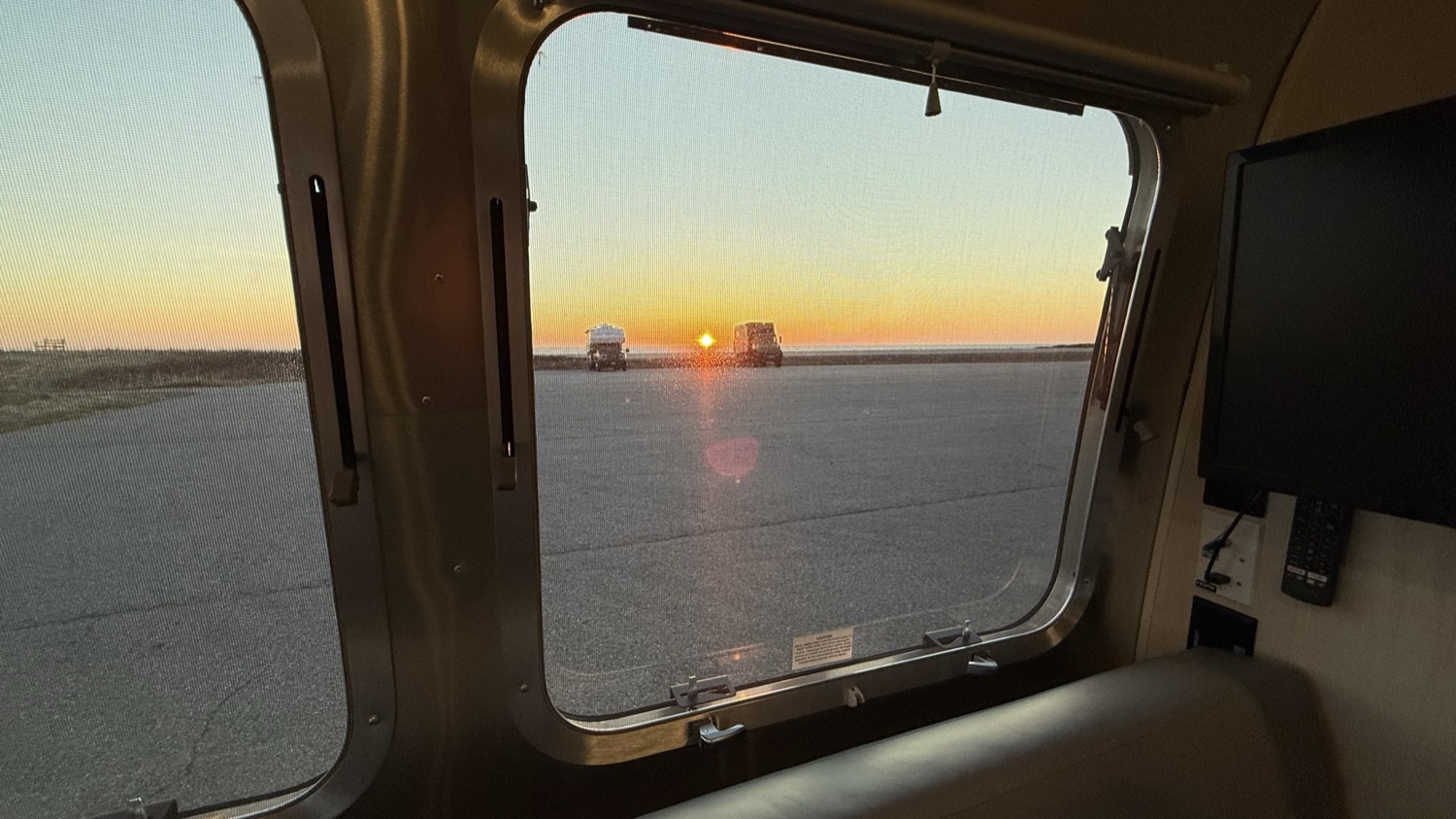 Sunset view of parked RVs seen through the Airstream's own window screen